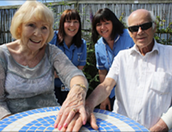 two elderly patients holding hands with two nurses in the background