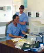 Two staff in blue uniforms at a computer.