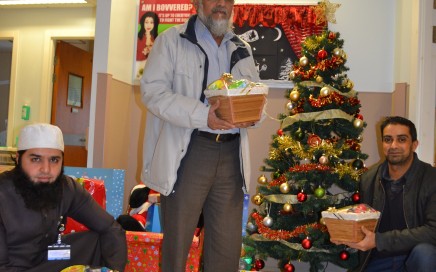 Three men with Christmas hampers next to a Christmas tree on a hospital ward