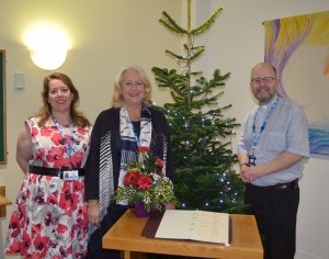 A chaplain and two women standing next to a Christmas tree