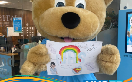 Blue Skies mascot bear holding a children's drawing