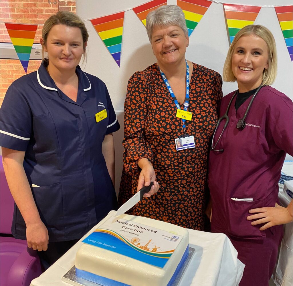 Nurses smiling and about to cut a cake for the first anniversary